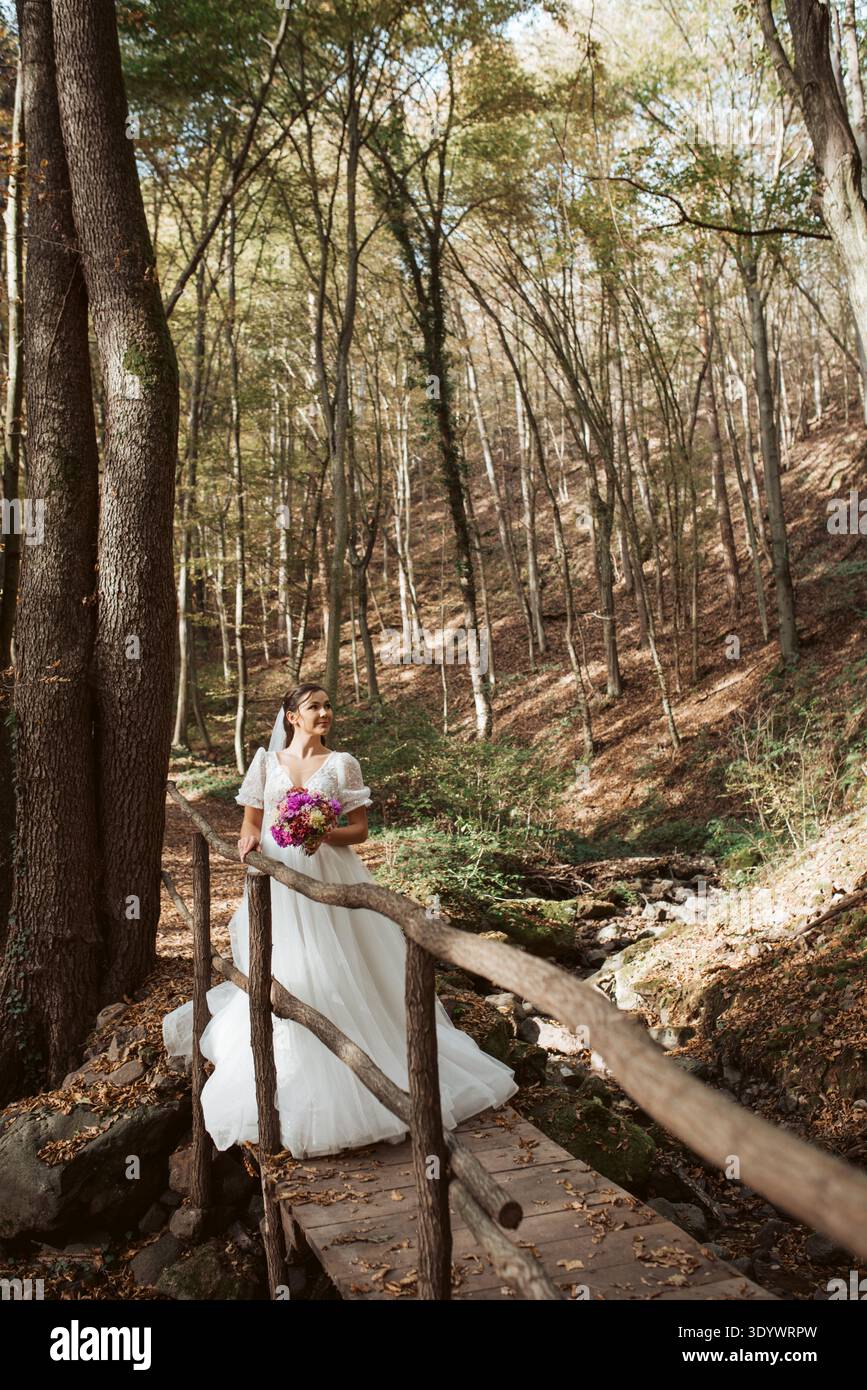 Mariée dans une robe de mariée blanche comme neige dans la nature, entourée d'une forêt. Banque D'Images