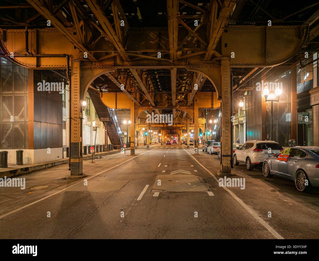 Downtown Chicago Street sous les voies ferrées l surélevées la nuit avec un éclairage chaud et des voitures garées Banque D'Images