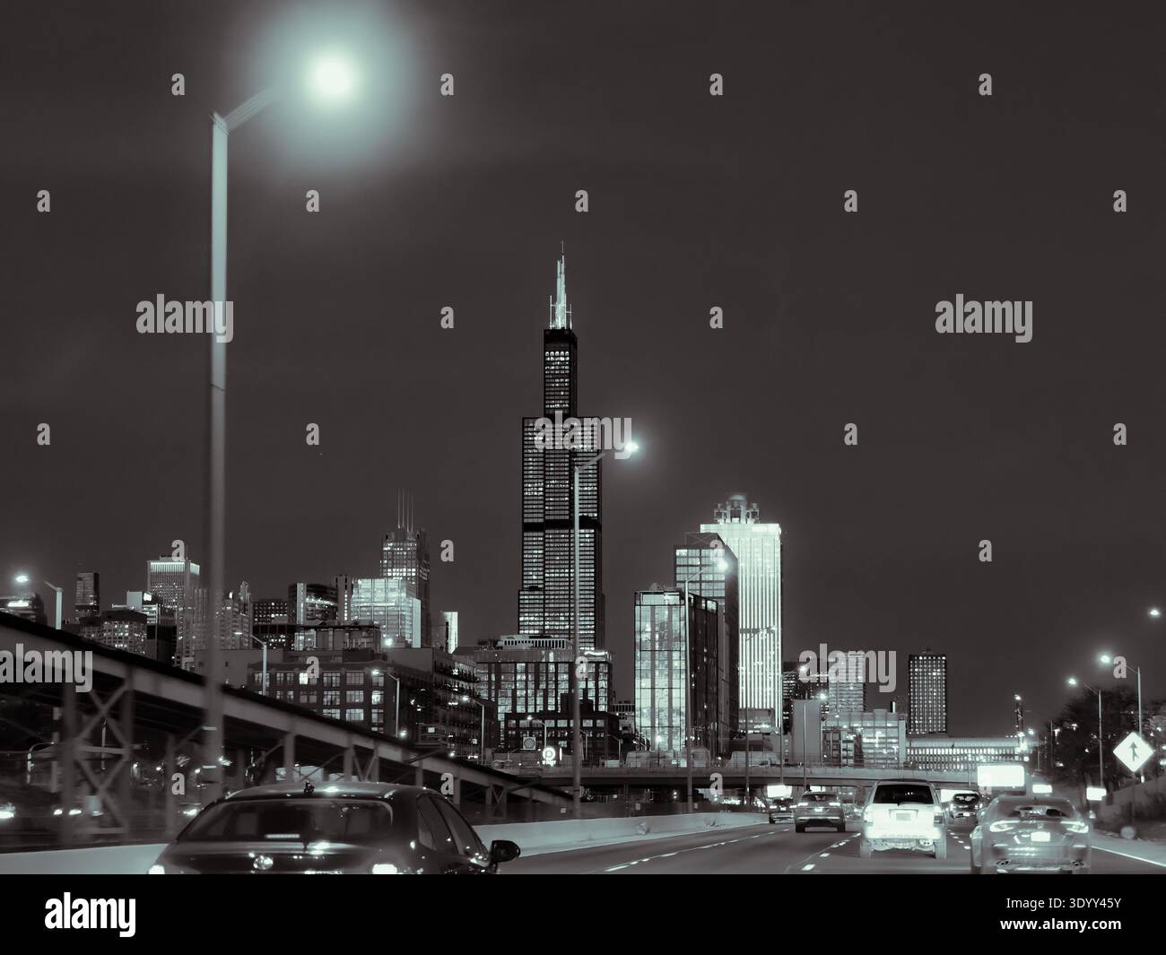 Vue nocturne de Willis Tower et de Chicago illuminée le long de l'autoroute I‑290 avec la circulation urbaine au premier plan Banque D'Images