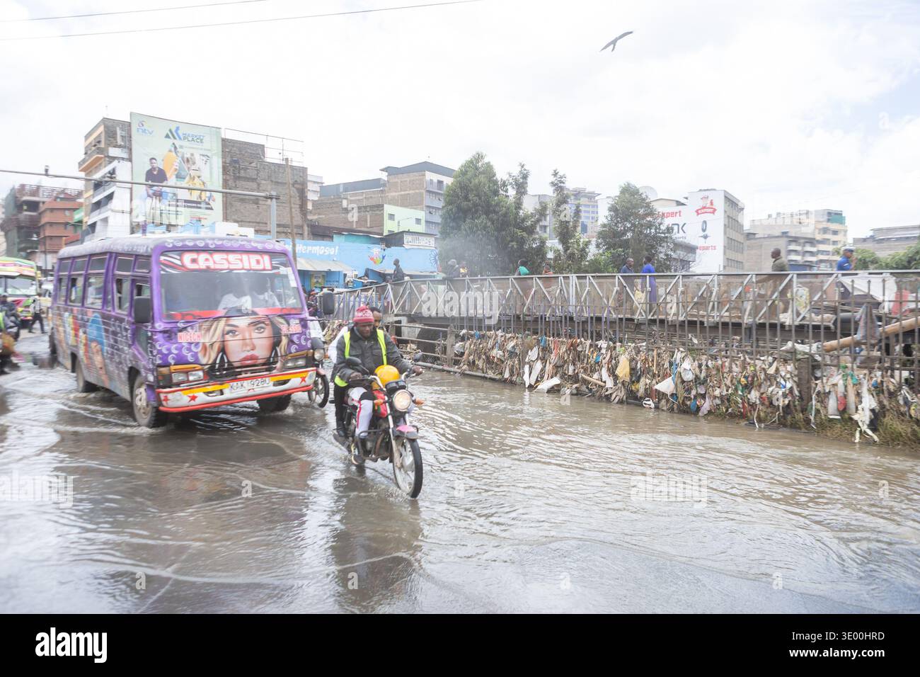Un motocycliste et un minibus public traversent les eaux de crue le long de Grogan Road près de la rivière Nairobi après une inondation qui a perturbé les entreprises de la région. De fortes pluies ont frappé Nairobi, Kenya, le vendredi 6 mars 2026, déclenché des crues soudaines qui ont submergé les routes et les systèmes de drainage, laissant des parties de la ville submergées et endommageant les entreprises et les véhicules à moteur. À Grogan Road, une plaque tournante très fréquentée pour les pièces de véhicules d'occasion près de la rivière Nairobi, les mécaniciens et les négociants ont continué à récupérer les pièces utilisables après que les inondations ont balayé les garages en bordure de route, les magasins de pièces détachées et les stands le long de la route. Banque D'Images