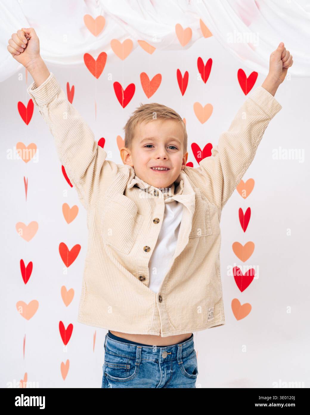 Enfant souriant heureux avec les mains levées entourées de cœurs rouges sur fond blanc. Joie, amour, émotions positives et concept de bonheur infantile Banque D'Images