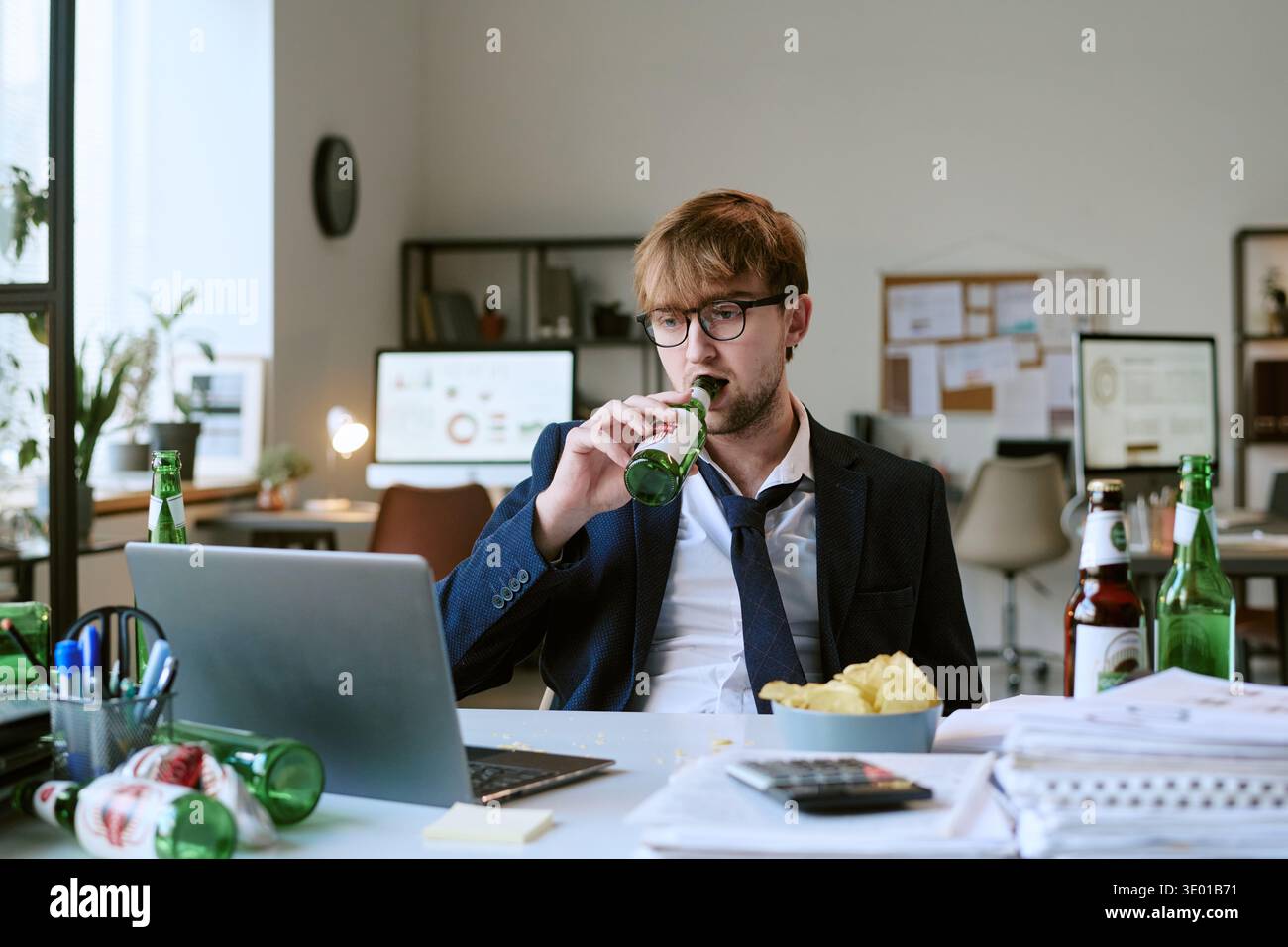 Jeune homme caucasien buvant de la bière tout en travaillant au bureau avec ordinateur portable Banque D'Images