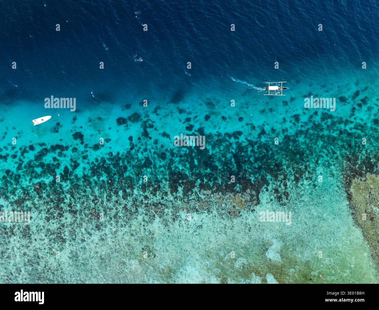 Vue aérienne par drone de bateaux naviguant au-dessus de récifs coralliens tropicaux peu profonds et d'eaux bleues profondes Banque D'Images