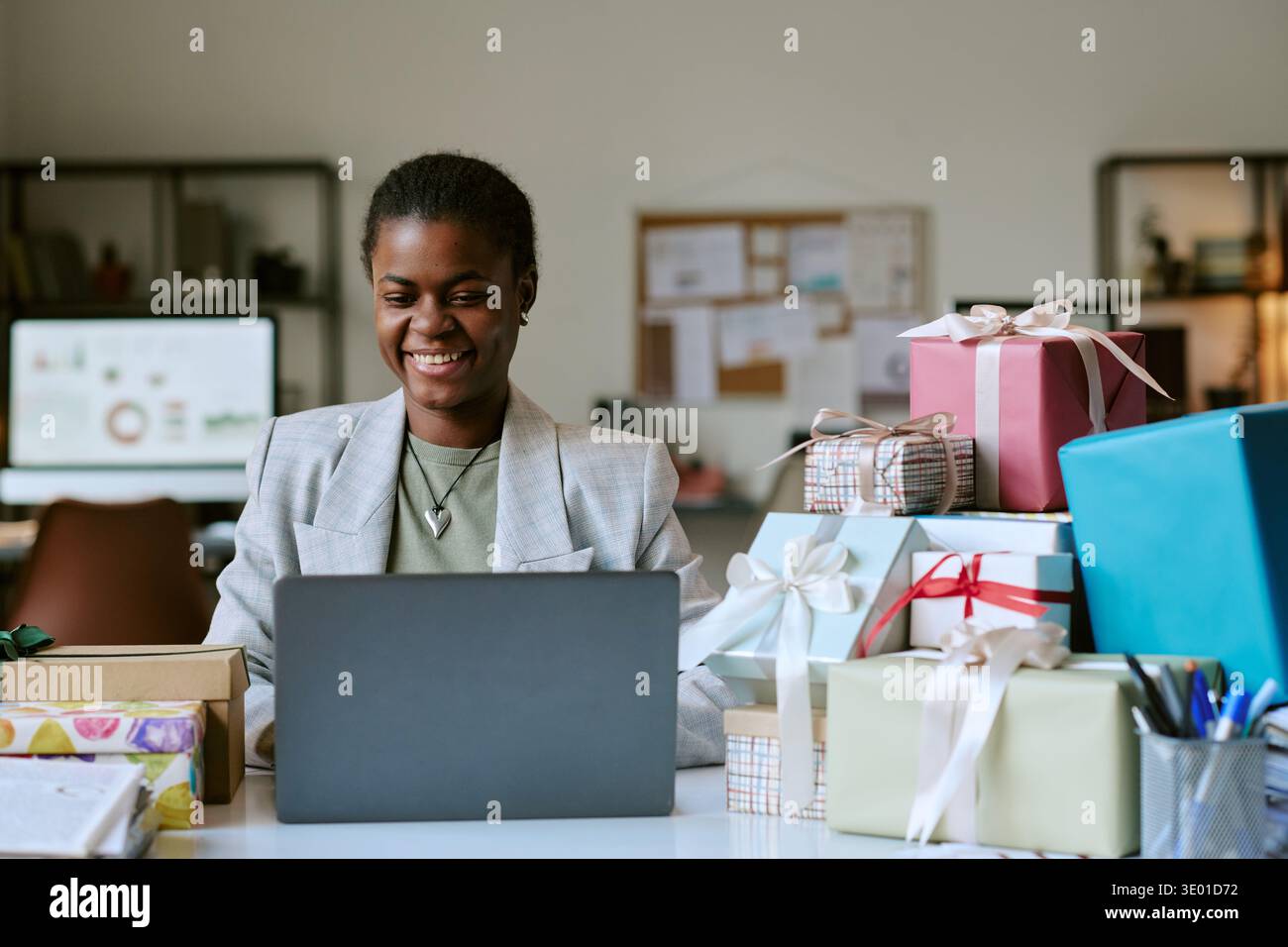 Jeune adulte femme noire souriante tout en travaillant sur ordinateur portable entouré de cadeaux Banque D'Images