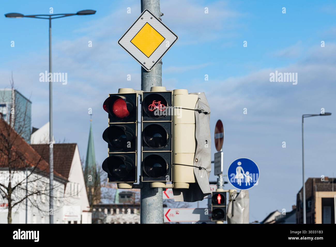 Les feux de circulation affichent des signaux rouges pour les voitures et les vélos dans un quartier animé de la ville. Un panneau piéton est à proximité, indiquant un passage sûr. Le ciel est le plus Banque D'Images