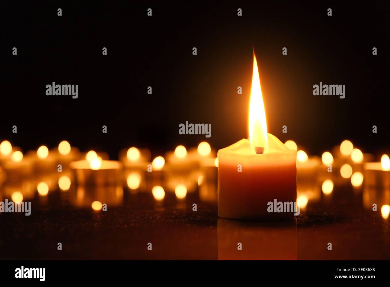 Allumer des bougies comme symbole de religion ou de deuil en temps de guerre. Une grande flamme de bougie devant des flammes défocalisées dans le noir noir et noir arrière Banque D'Images