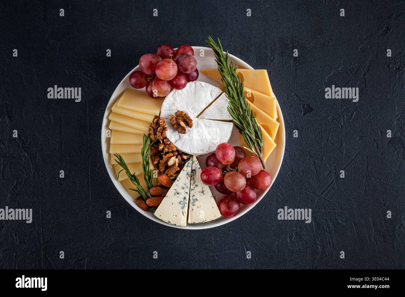 Un plateau de fromages magnifiquement arrangé présente une variété de fromages, y compris doux et bleus, garnis de raisins frais, de noix croquantes et aromatiques Banque D'Images