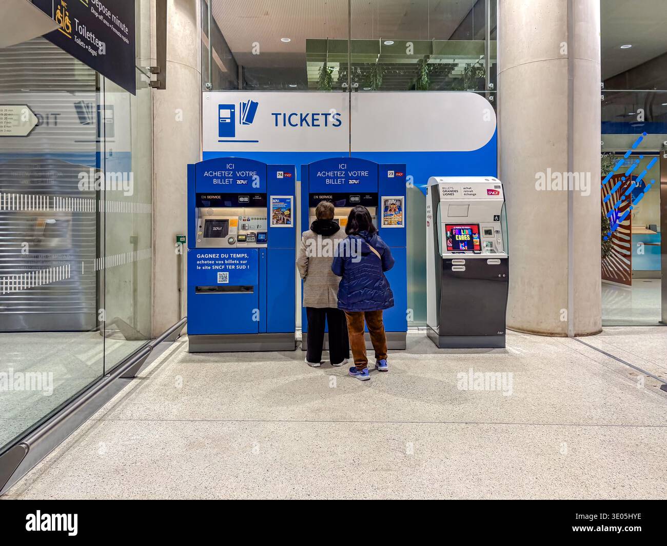 Distributeurs automatiques de billets à la gare de Monaco Monte-Carlo, France. Deux voyageurs achètent des billets auprès de SNCF Zou ! machines dans un environnement de transit moderne. Banque D'Images