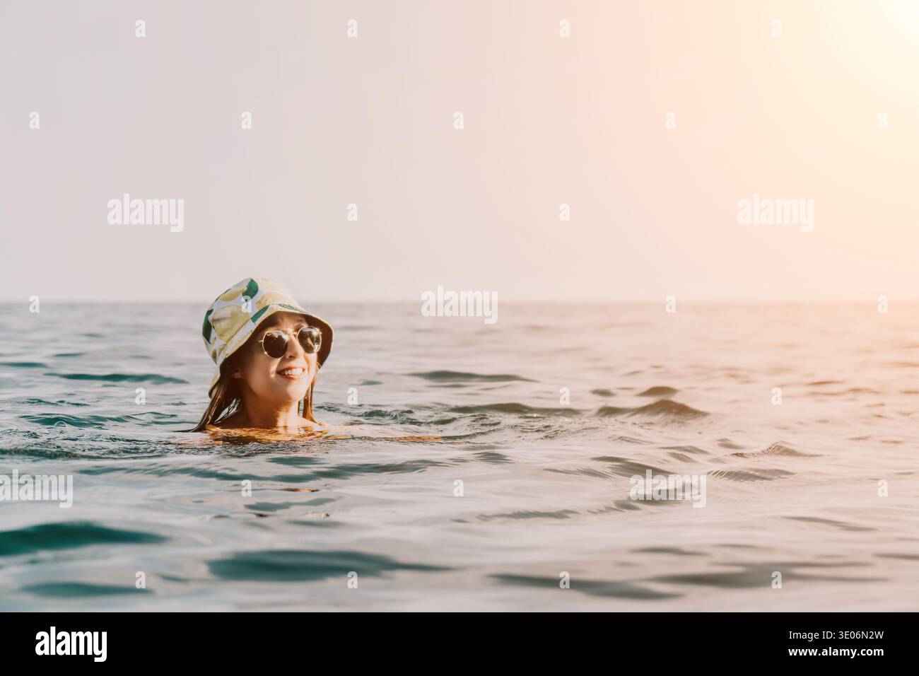 Femme natation Ocean Beach Summer - Une femme portant un chapeau et des lunettes de soleil nage dans l'océan par une journée ensoleillée. Banque D'Images