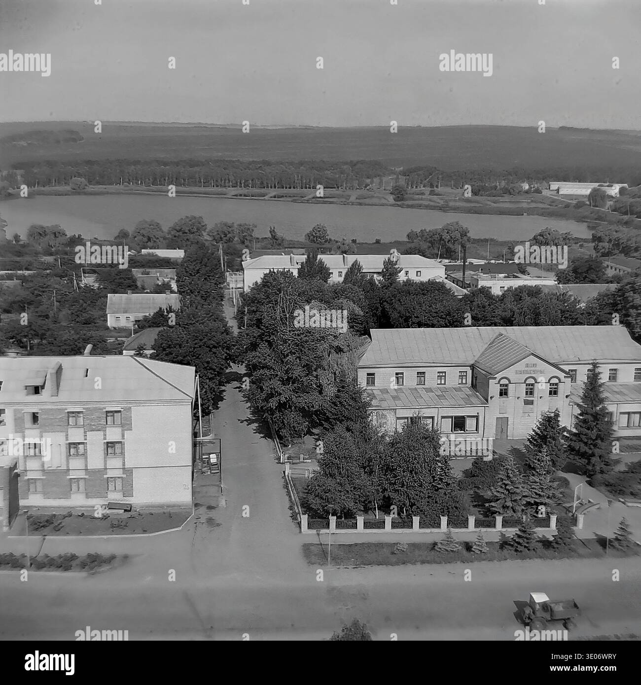 Une vaste photographie vintage en noir et blanc des années 1980 présente une vue imprenable sur le quartier résidentiel et culturel central de l'entreprise Donrybkombinat dans le quartier de Slavyansk. La perspective aérienne panoramique capture l'éminente Maison de la culture, les immeubles d'habitation environnants et les arbres verdoyants avec pour toile de fond un vaste réservoir tranquille. Ce paysage authentique préserve magnifiquement l'infrastructure communautaire et la vie quotidienne dans le Donbass paisible avant la guerre. Banque D'Images