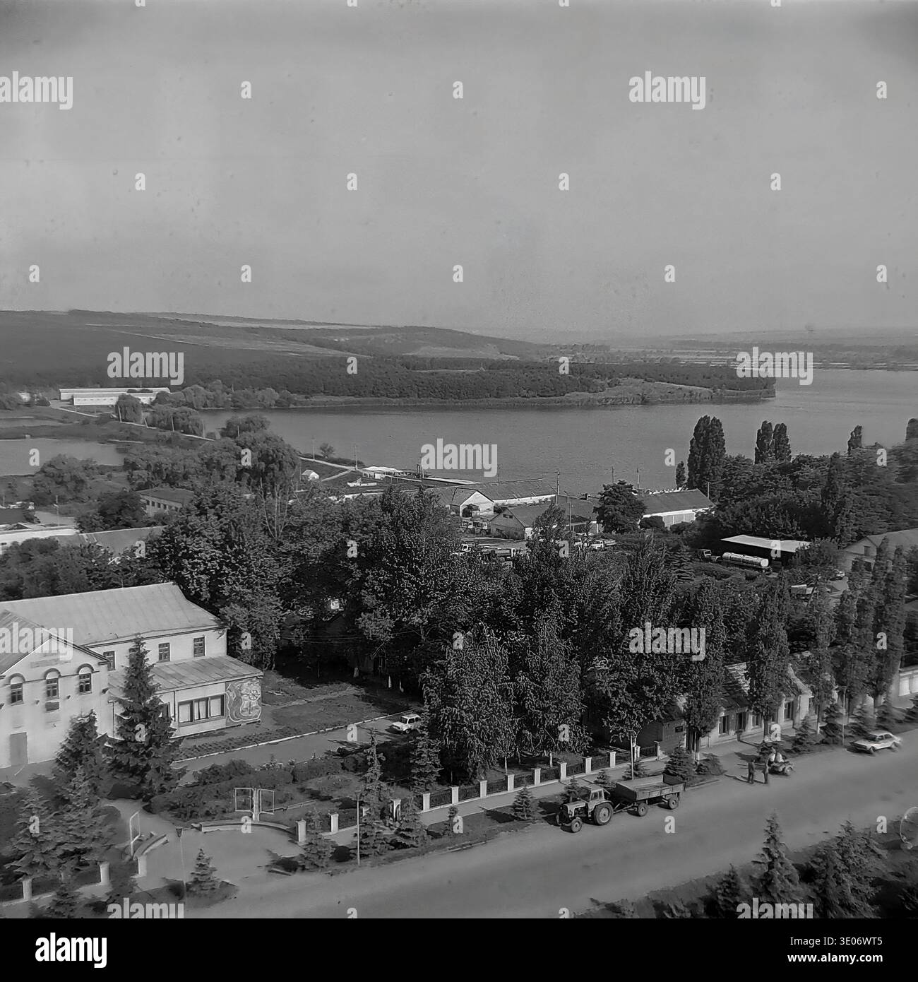 Une vaste photographie vintage en noir et blanc des années 1980 présente une vue imprenable sur le quartier résidentiel et culturel central de l'entreprise Donrybkombinat dans le quartier de Slavyansk. La perspective aérienne panoramique capture l'éminente Maison de la culture, les immeubles d'habitation environnants et les arbres verdoyants avec pour toile de fond un vaste réservoir tranquille. Ce paysage authentique préserve magnifiquement l'infrastructure communautaire et la vie quotidienne dans le Donbass paisible avant la guerre. Banque D'Images