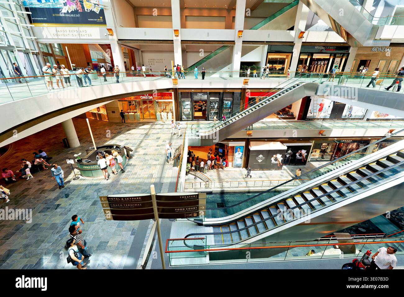 Les acheteurs parcourent les magasins du Marina Bay Sands Mall à Singapour. Les escaliers mécaniques et les panneaux aident à guider les visiteurs dans l'espace occupé. Banque D'Images