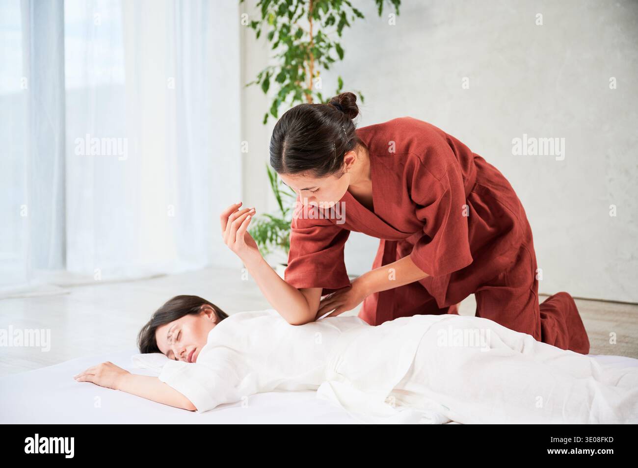 Masseuse faisant massage yoga thaïlandais. Thérapeute de femme faisant le traitement de massage traditionnel pour la patiente féminine utilisant le coude. Client allongé sur tapis, méditant, profitant d'un massage des mains dans une atmosphère calme. Banque D'Images