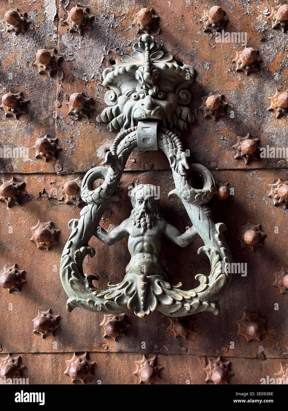 Frappeur de porte Triton en bronze orné sur une porte en bois fortement rouillée et cloutée au Palais des Doges, Gênes, Italie. Banque D'Images