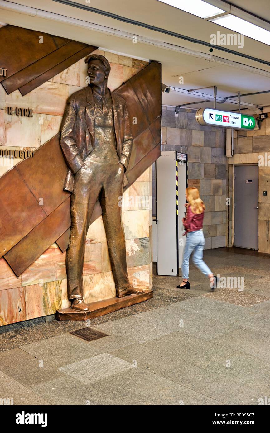 Une personne passe devant une statue de bronze à la station de métro Mayakovskaya à Saint-Pétersbourg. La station affiche un design unique et une atmosphère animée. Banque D'Images