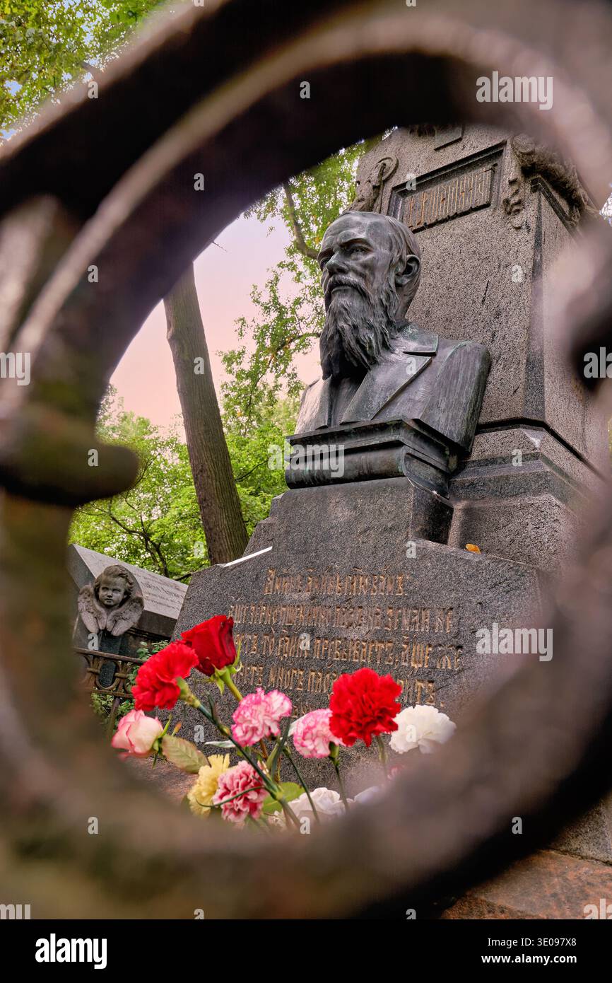 Les gens visitent la tombe de Fyodor Dostoïevski dans le cimetière de Tikhvin. Les fleurs sont placées près de la tombe parmi les arbres et la verdure. Banque D'Images