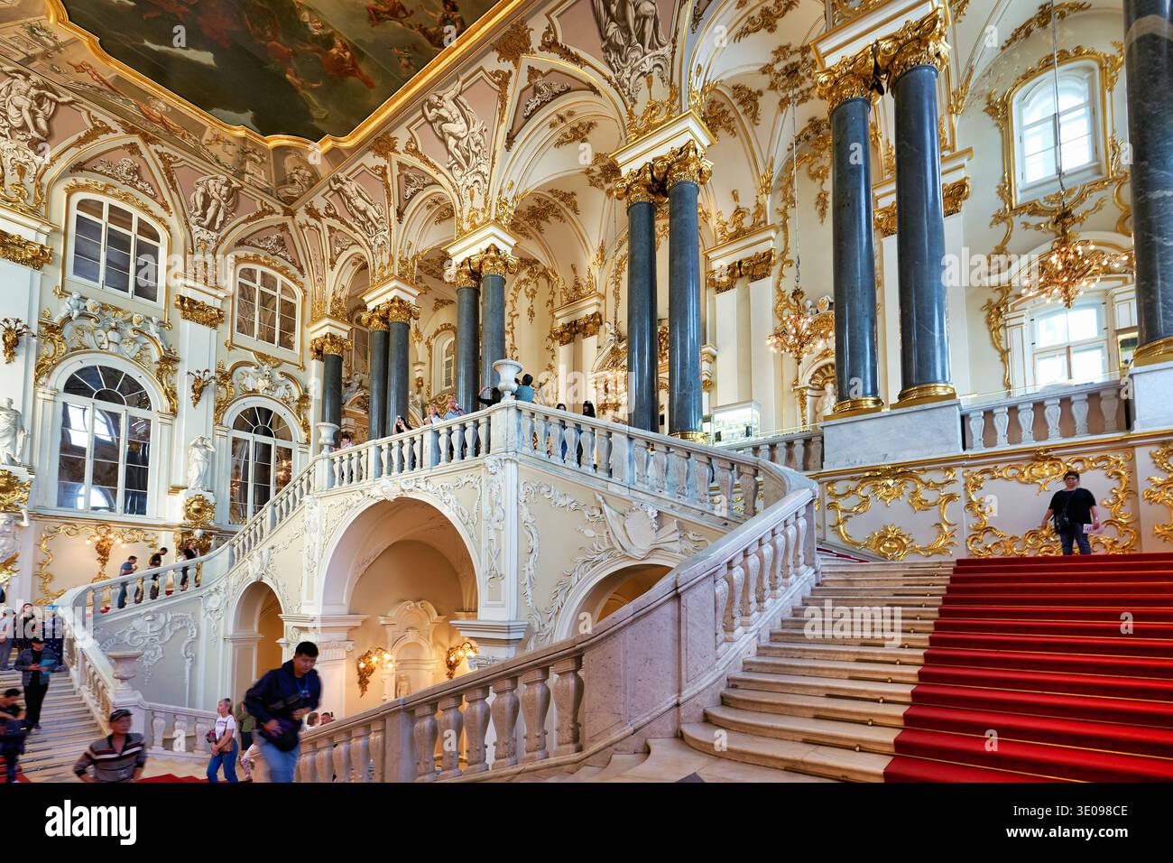 Les visiteurs montent l'escalier du Jourdain dans le Palais d'hiver. Les hautes colonnes et les détails ornés les entourent. Banque D'Images