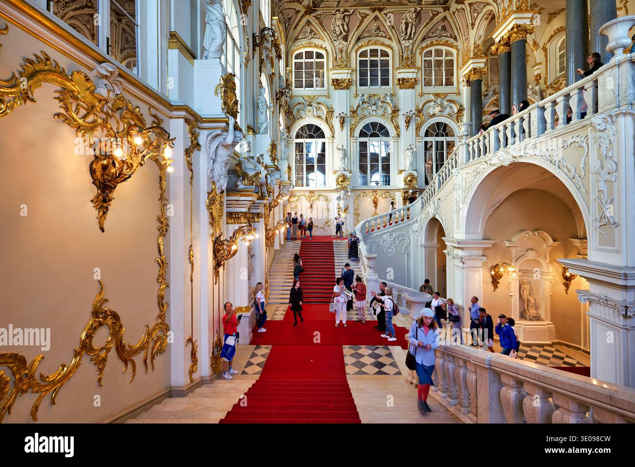 Les gens marchent sur les escaliers du tapis rouge dans l'escalier Jourdain du Palais d'hiver. Les visiteurs admirent l'architecture ornée et les détails. Banque D'Images