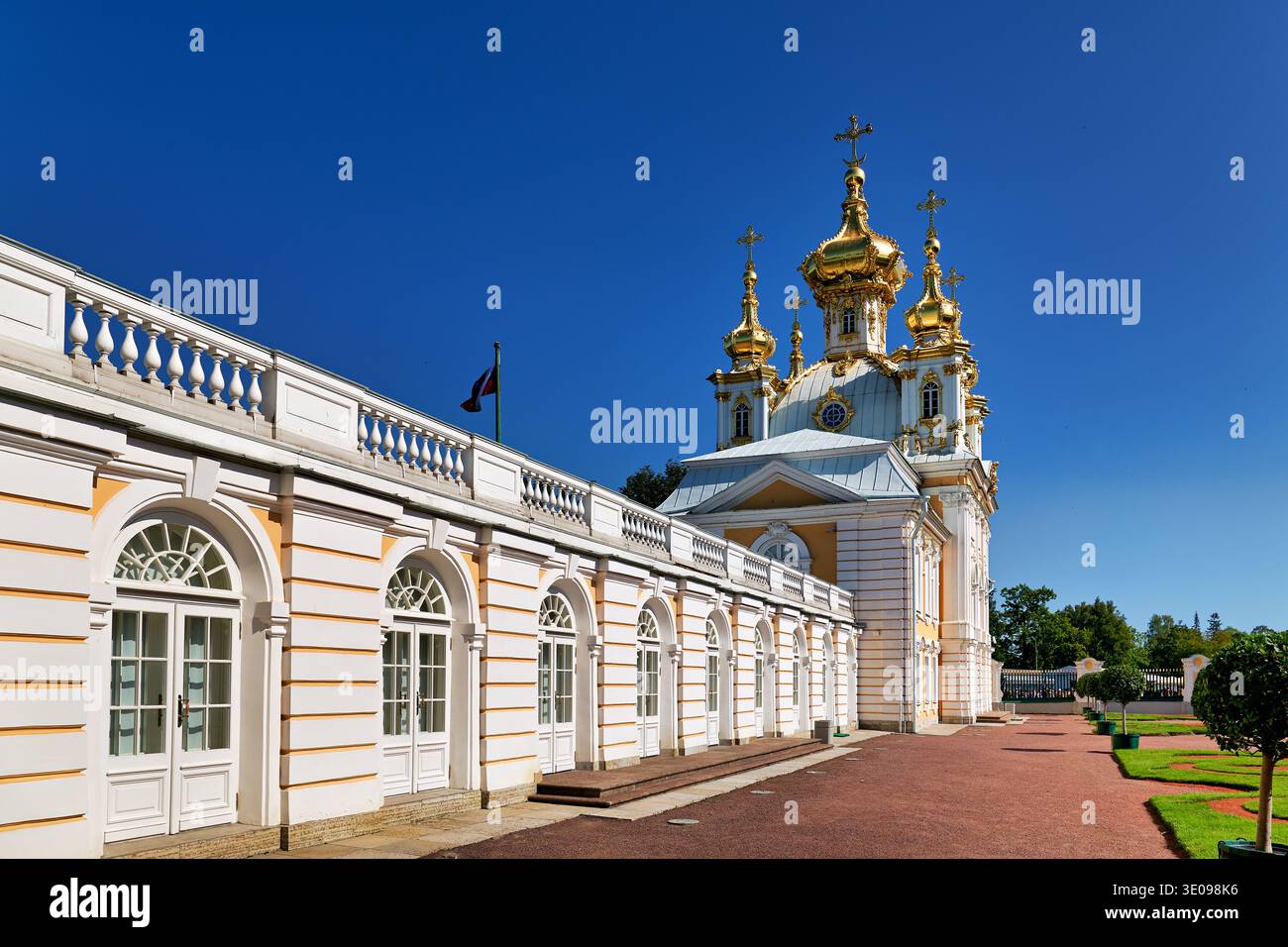 Les visiteurs marchent près des dômes dorés du palais de Peterhof à Saint-Pétersbourg. Le ciel lumineux offre une vue dégagée sur le site historique. Banque D'Images