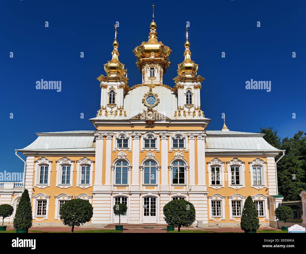 Les touristes explorent le Palais Peterhof à Saint-Pétersbourg, Russie. Le bâtiment présente des dômes dorés et une architecture détaillée sous un ciel bleu clair. Banque D'Images