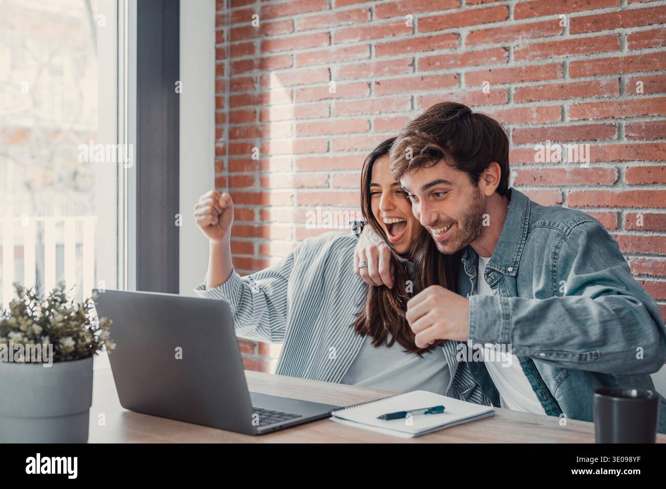 Un couple millennial ravi assis au bureau regarder l'écran d'ordinateur portable se sentir euphorique avec la victoire en ligne, heureux jeune mari et femme excité lire de bonnes nouvelles, obtenir Banque D'Images