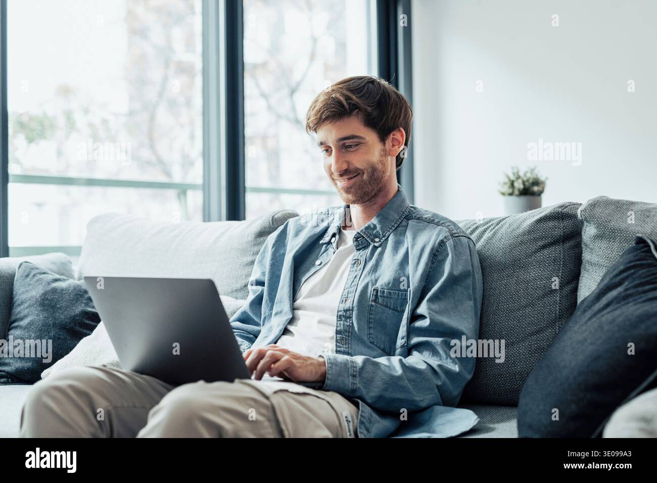 Bel homme sérieux est assis sur le canapé avec l'ordinateur sur les tours, passer du temps à la maison des informations de navigation sur le Web, utiliser la technologie moderne, faire l'ordre sur Internet. Freelanc Banque D'Images