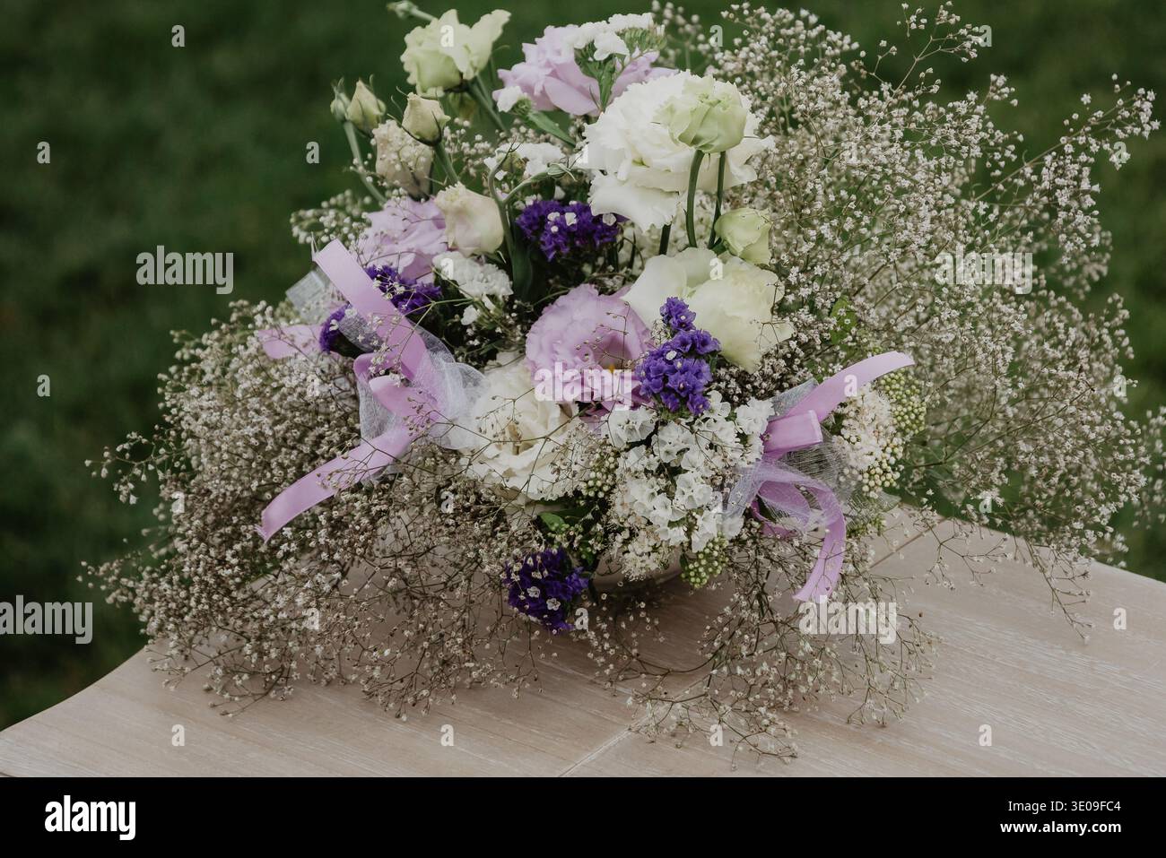 Pièce maîtresse romantique à fleurs pastel avec roses, lisianthus, statice et souffle de bébé disposés dans un récipient rustique sur une table en bois à l’extérieur. E Banque D'Images