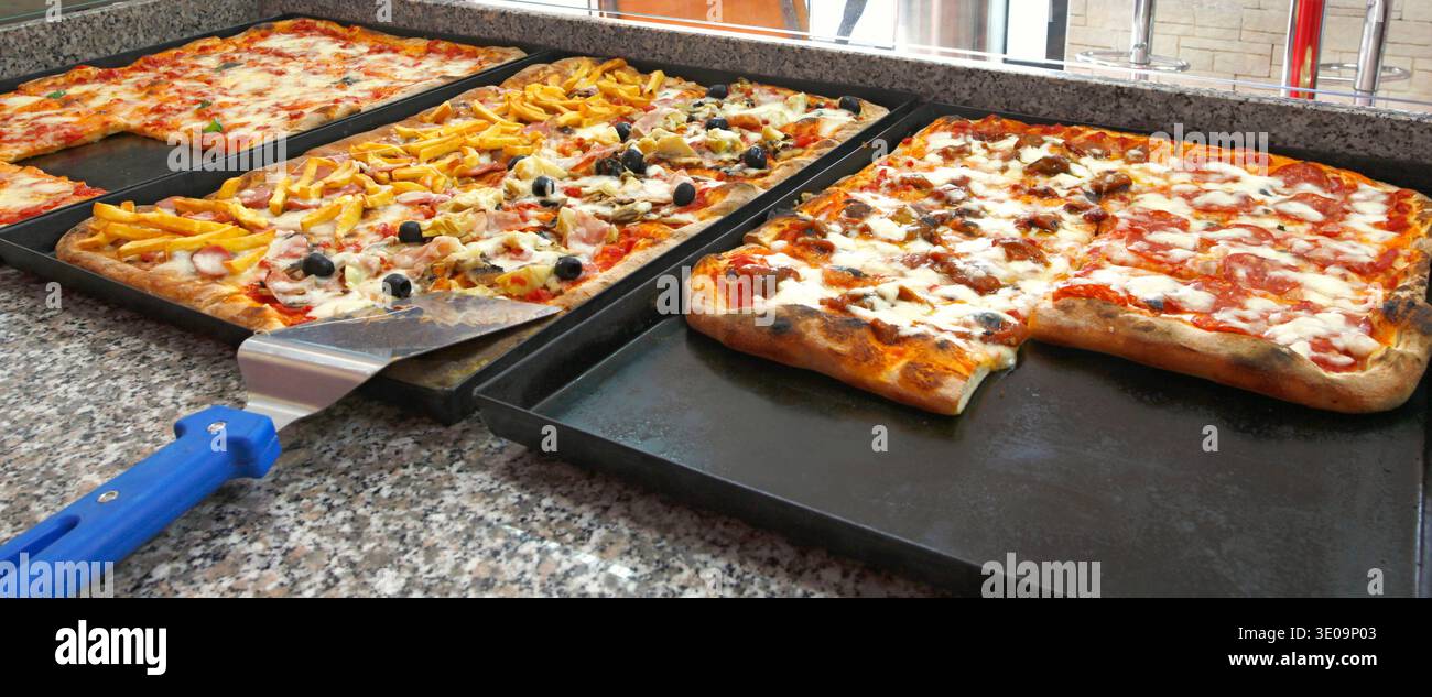 Comptoir de la pizzeria avec bacs et morceaux carrés de pizza. Banque D'Images
