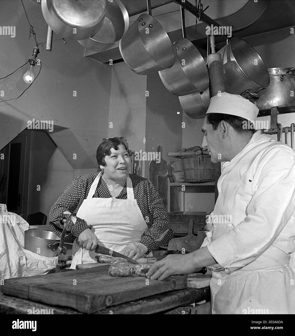 Fête familiale de la Saint-Sylvestre de la famille Di Costanzo, New York, 1942. La photo montre la famille Di Costanzo, propriétaire du restaurant Marconi, célébrant le nouvel an dans leur maison. Mamma est photographiée supervisant la cuisson du dîner de vacances dans la cuisine, soulignant à la fois les traditions familiales et le rôle central de la préparation des aliments dans les ménages italo-américains. L'image capture la vie domestique, la culture familiale immigrée et les coutumes sociales à New York au début des années 1940, dans le contexte de la première Guerre mondiale Banque D'Images