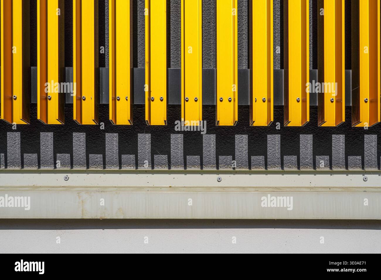 Lattes verticales jaunes rythmées, façade Stadthalle Cham projetant un motif d'ombre géométrique symétrique sur le mur en dessous. Cham, Bavière, Allemagne Banque D'Images