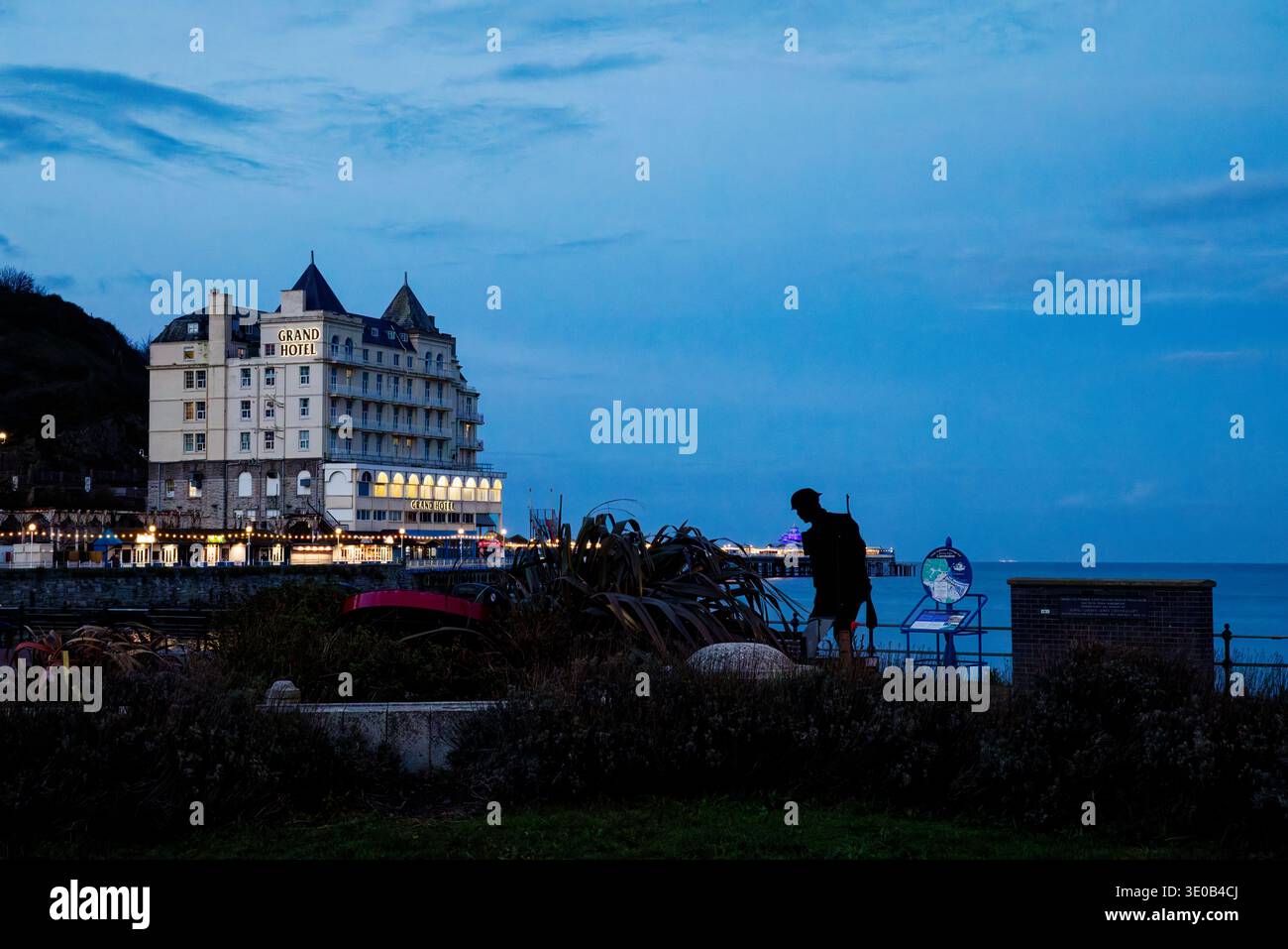 Les lumières du Grand Hôtel et de la jetée brillent dans la lumière sombre de la soirée à l'horloge florale sur le front de mer de Llandudno, dans le nord du pays de Galles. Banque D'Images