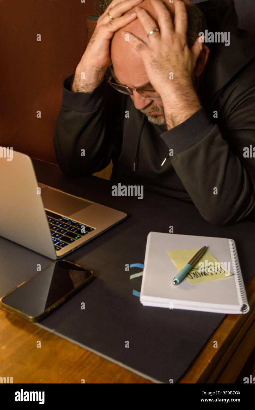 Homme stressé à un ordinateur portable avec smartphone, ordinateur portable et mot de passe note, image conceptuelle de cyber incident, problèmes de mot de passe, perte de compte et numérique Banque D'Images