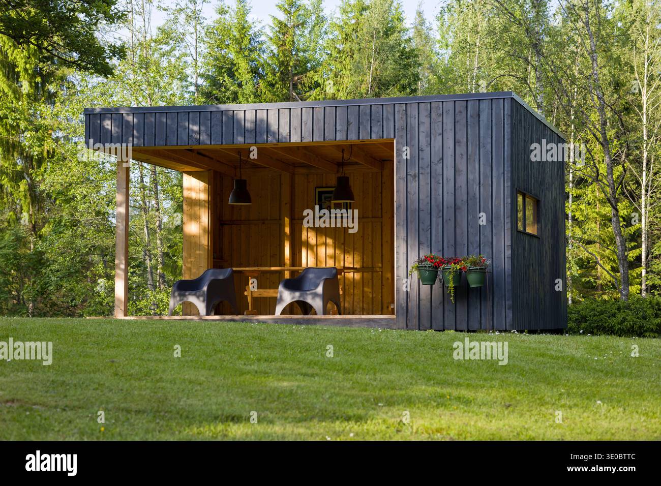 Un élégant abri en bois se trouve dans une clairière verdoyante, avec des sièges confortables et des plantes suspendues. La lumière du soleil projette des ombres douces sur l'invitante sp Banque D'Images