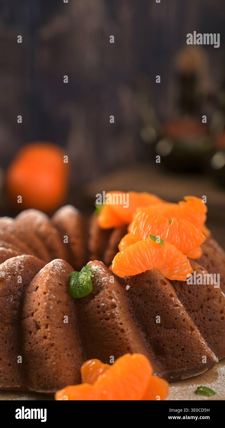 Un gros plan en grand angle met l'accent sur la texture complexe d'un gâteau bundt brun doré. Des segments de mandarine éclatants et de minuscules feuilles de menthe garnissent le Banque D'Images