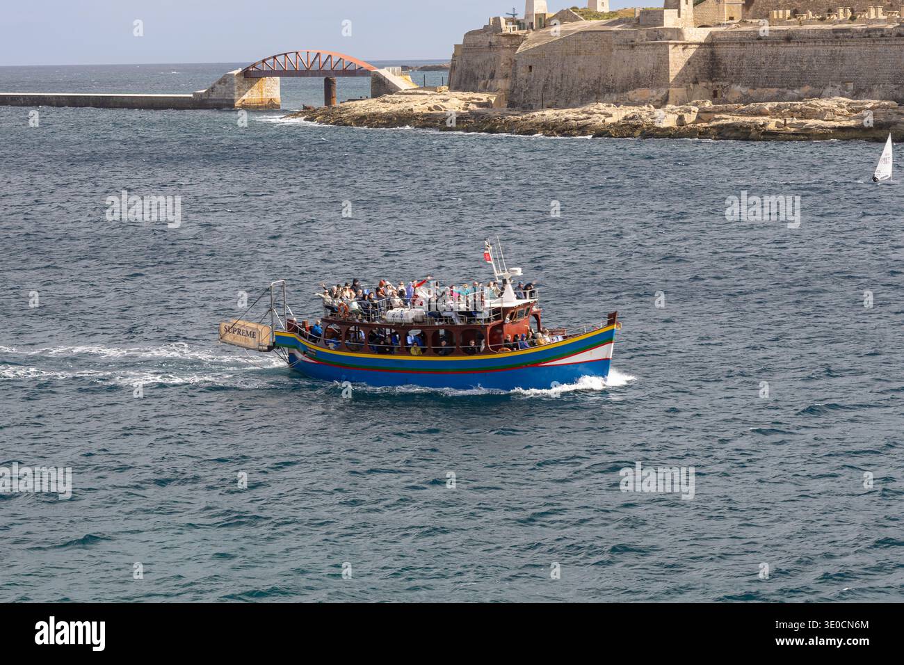 Valletta, Malte - 05 février 2026 : un bateau touristique traditionnel maltais haut en couleur qui passe devant le pont brise-lames Fort compris Elmo Banque D'Images