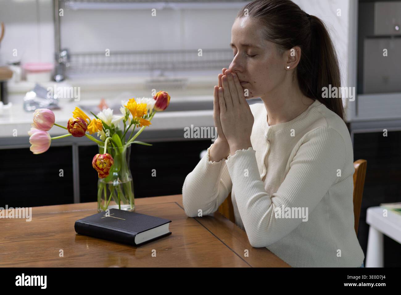 Séoul, Corée du Sud - 03.12.2026 : femme chrétienne priant avec la Sainte Bible et des fleurs printanières à la maison Banque D'Images