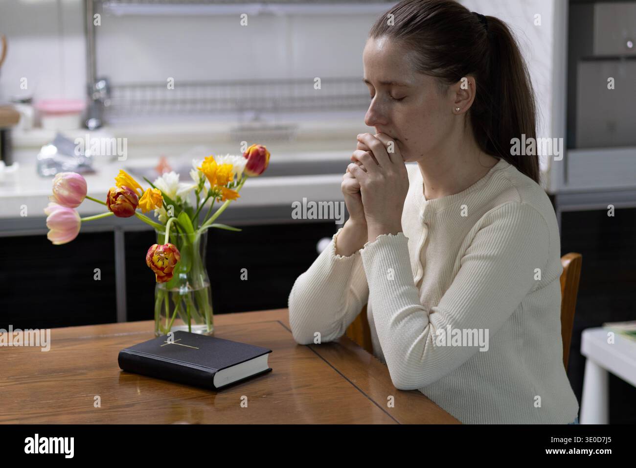 Séoul, Corée du Sud - 03.12.2026 : femme chrétienne priant avec la Sainte Bible et des fleurs printanières à la maison Banque D'Images