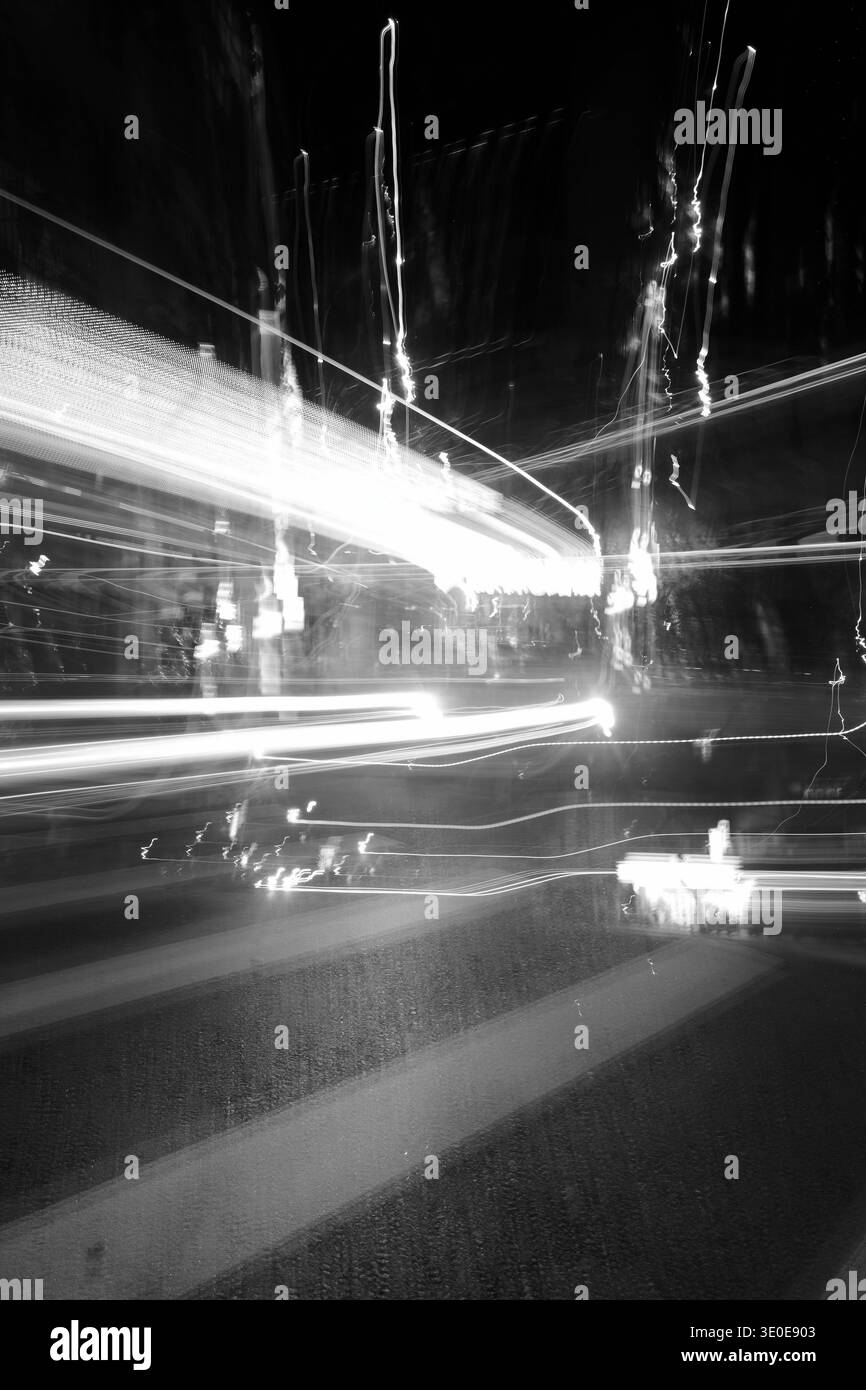 Artistique noir et blanc longue exposition de traînées de lumière de véhicule se tissant à travers un carrefour nocturne animé. Banque D'Images