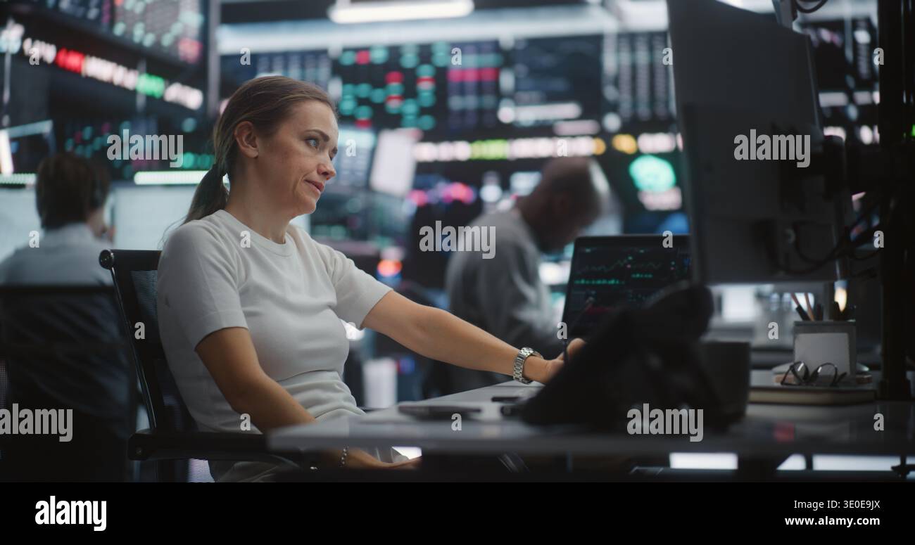 Tout en surveillant les indices de stock en temps réel, la spécialiste Tech Savvy femme enregistre la commande vocale ou la mise à jour sur téléphone mobile. Efficacité de la communication audio instantanée dans un hub d'échange sophistiqué. Banque D'Images