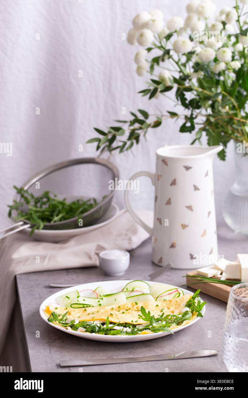 Omelette fraîchement cuite avec fromage feta et herbes, servie avec salade de radis et concombre sur une table de style ferme. Banque D'Images