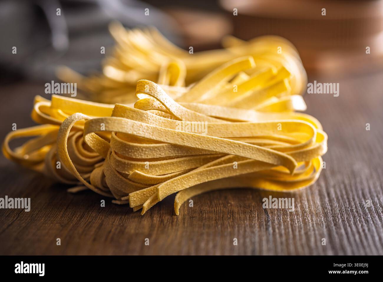 Les brins de pâtes fettuccine reposent sur une surface blanche, paraissant doux et frais. Ce type de pâtes est souvent utilisé dans divers plats. Banque D'Images