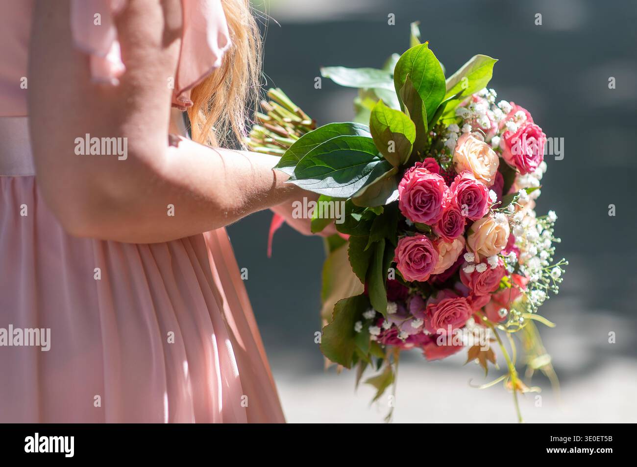 Jeune mariée adulte en robe beige tenant un bouquet de mariage vibrant à la lumière du soleil, composition florale élégante avec une humeur émotionnelle. Banque D'Images