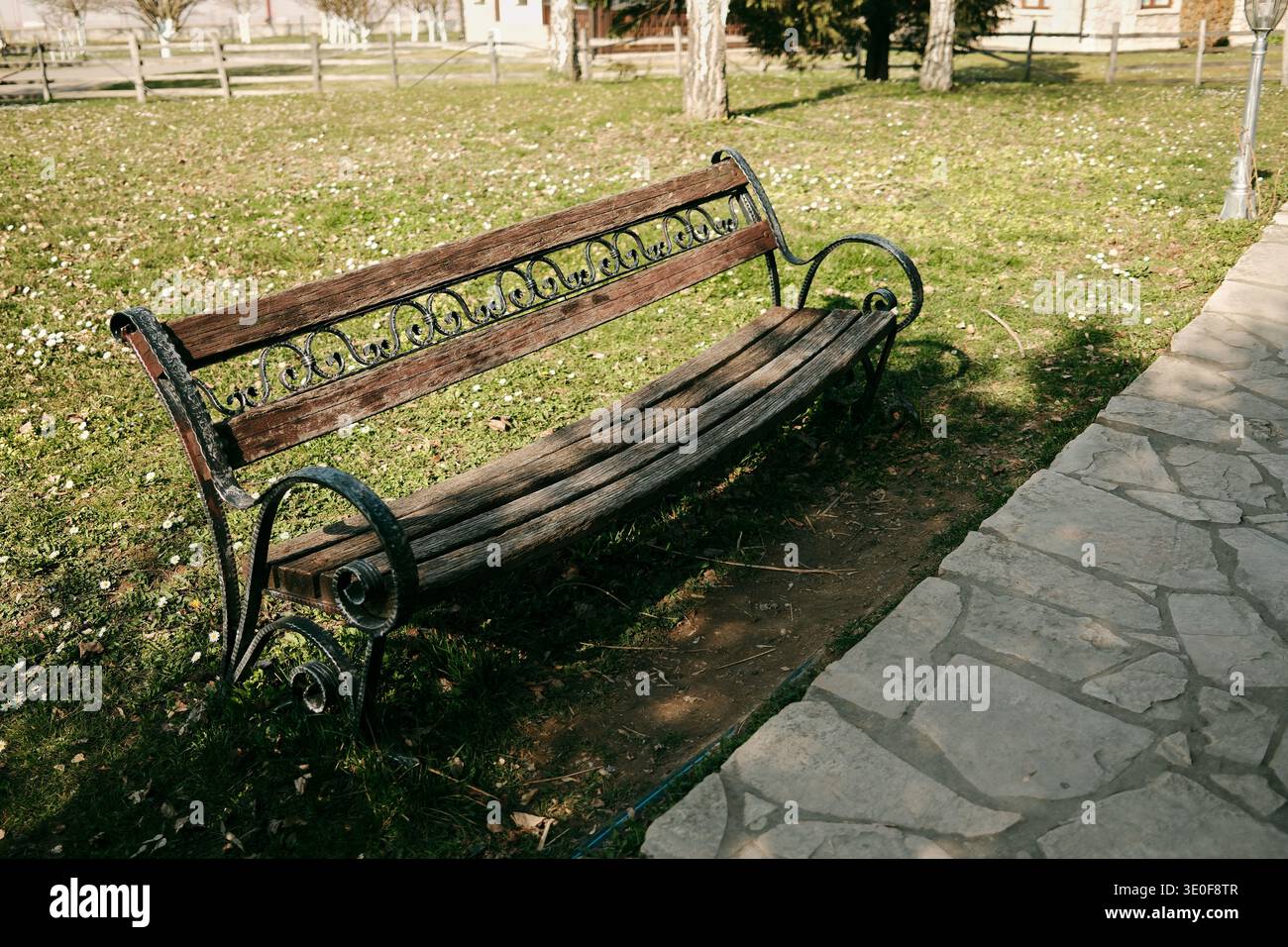 Ancienne banquette en bois avec cadre métallique décoratif posée à côté d'une allée en pierre dans un jardin de parc. Concept de détente, de loisirs en plein air et de paix Banque D'Images