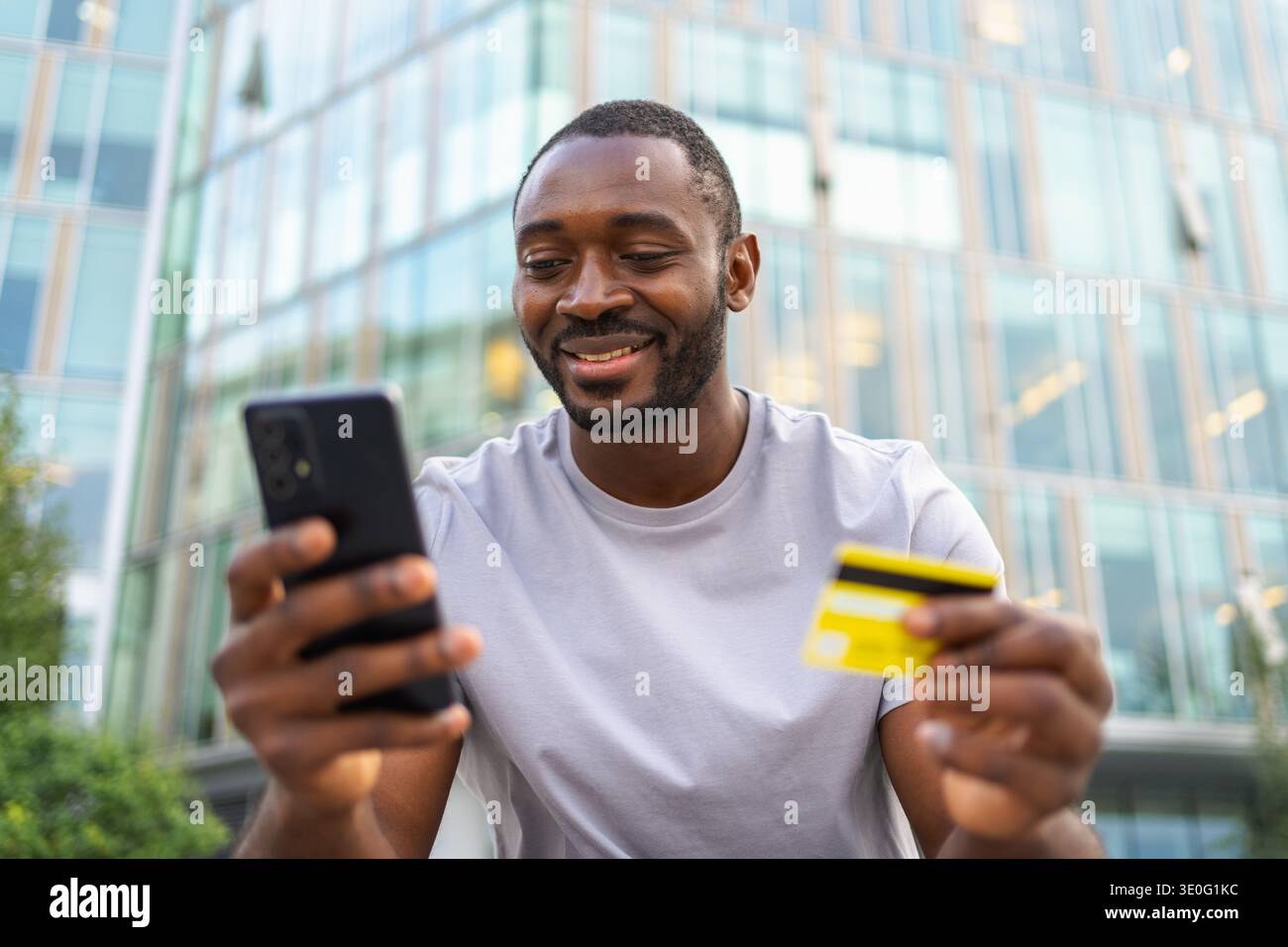 Homme africain magasinant en ligne tenant smartphone payant avec carte de crédit d'or. Guy sur la rue urbaine dans la ville achetant sur Internet entrer les détails de la carte de crédit. Service de livraison de commerce électronique d'achat en ligne Banque D'Images