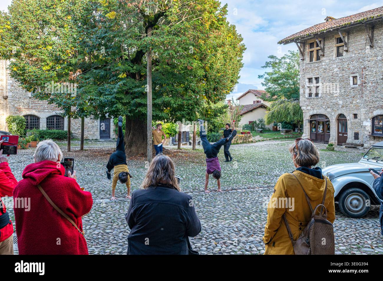 Les spectateurs regardent des artistes de rue faire des équilibres sur un carré pavé encadré par des maisons en pierre médiévales dans le village historique de Perouges, France Banque D'Images