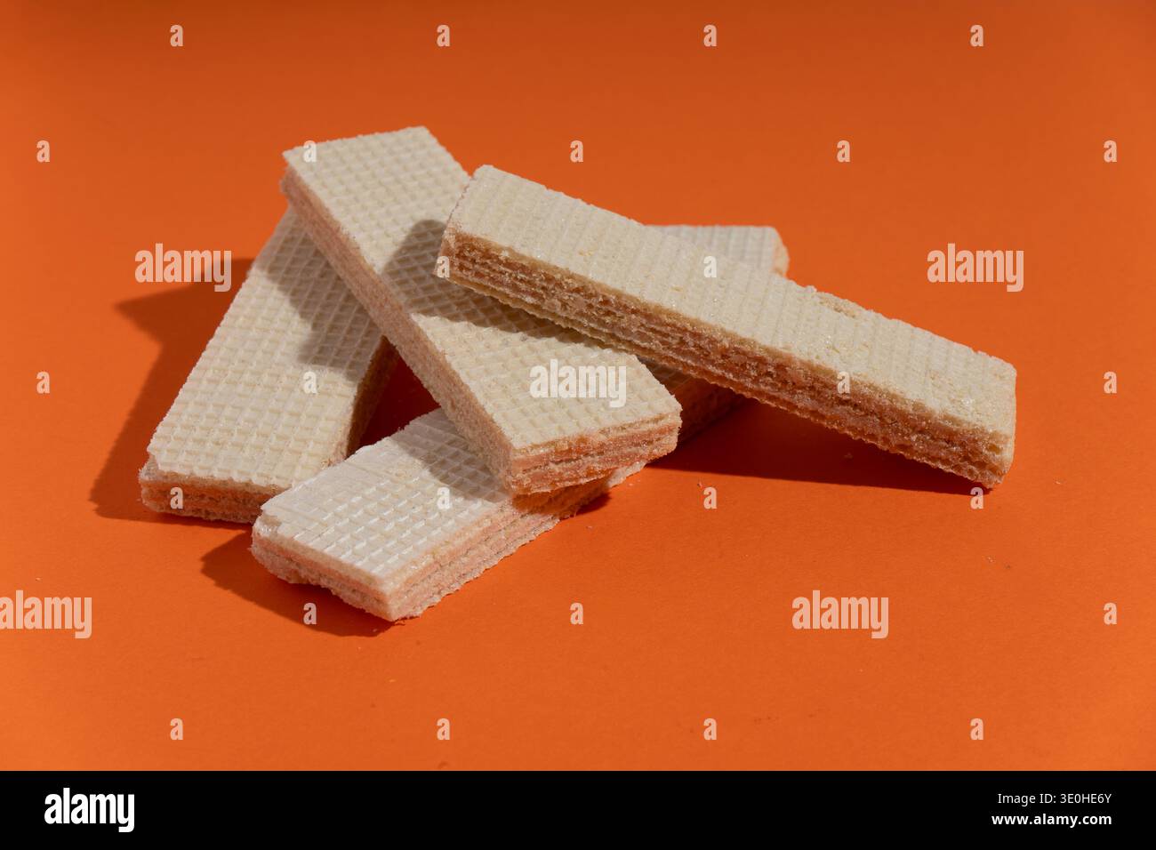 Gaufrettes sucrées et croquantes garnies de vanille, empilées sur un fond orange éclatant, représentant la commodité des collations et le plaisir simple Banque D'Images