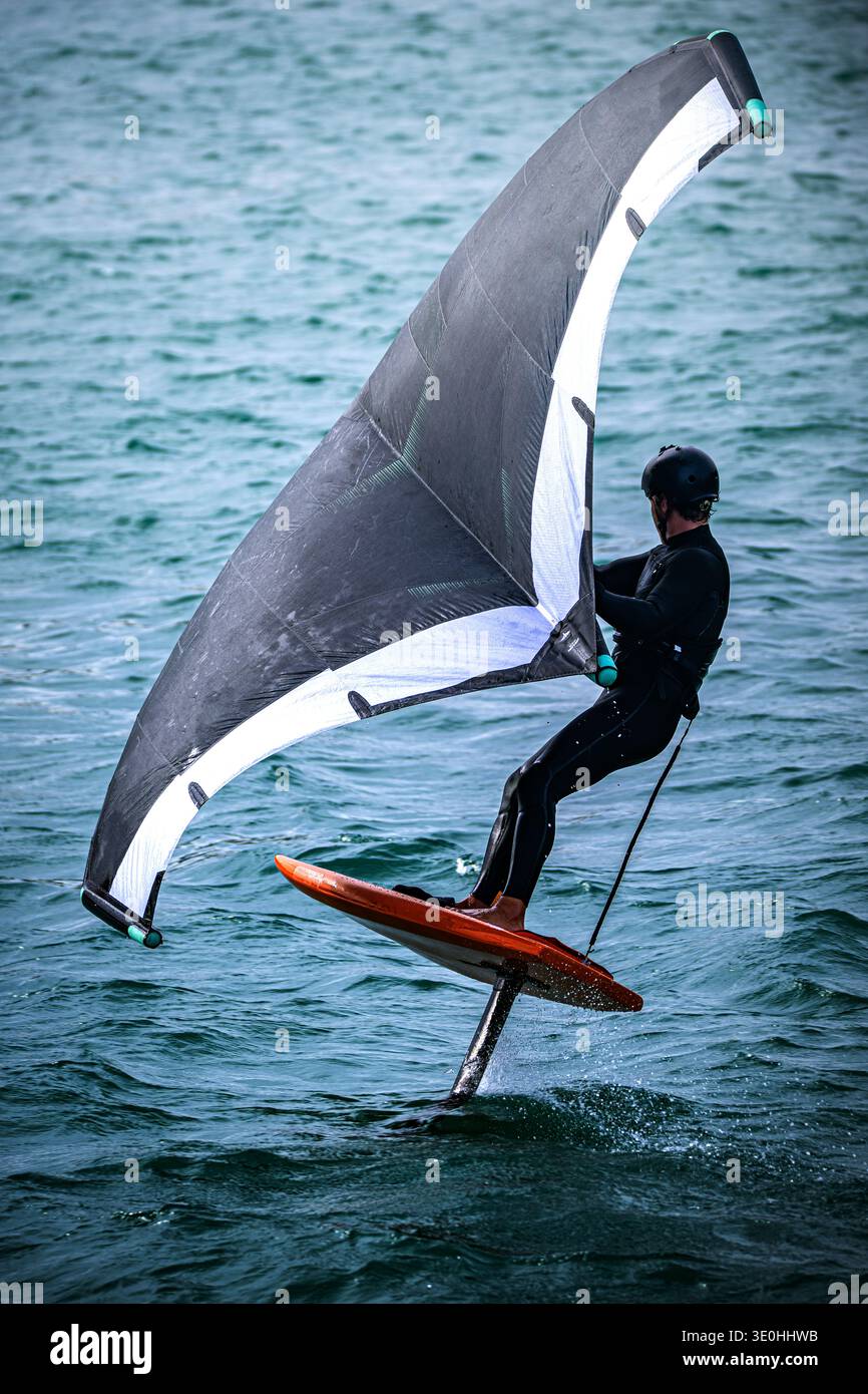 Une personne monte une planche unique avec une grande voile d'aile au-dessus de l'eau. Le cavalier s'équilibre sur la planche alors qu'il glisse au-dessus des vagues Banque D'Images