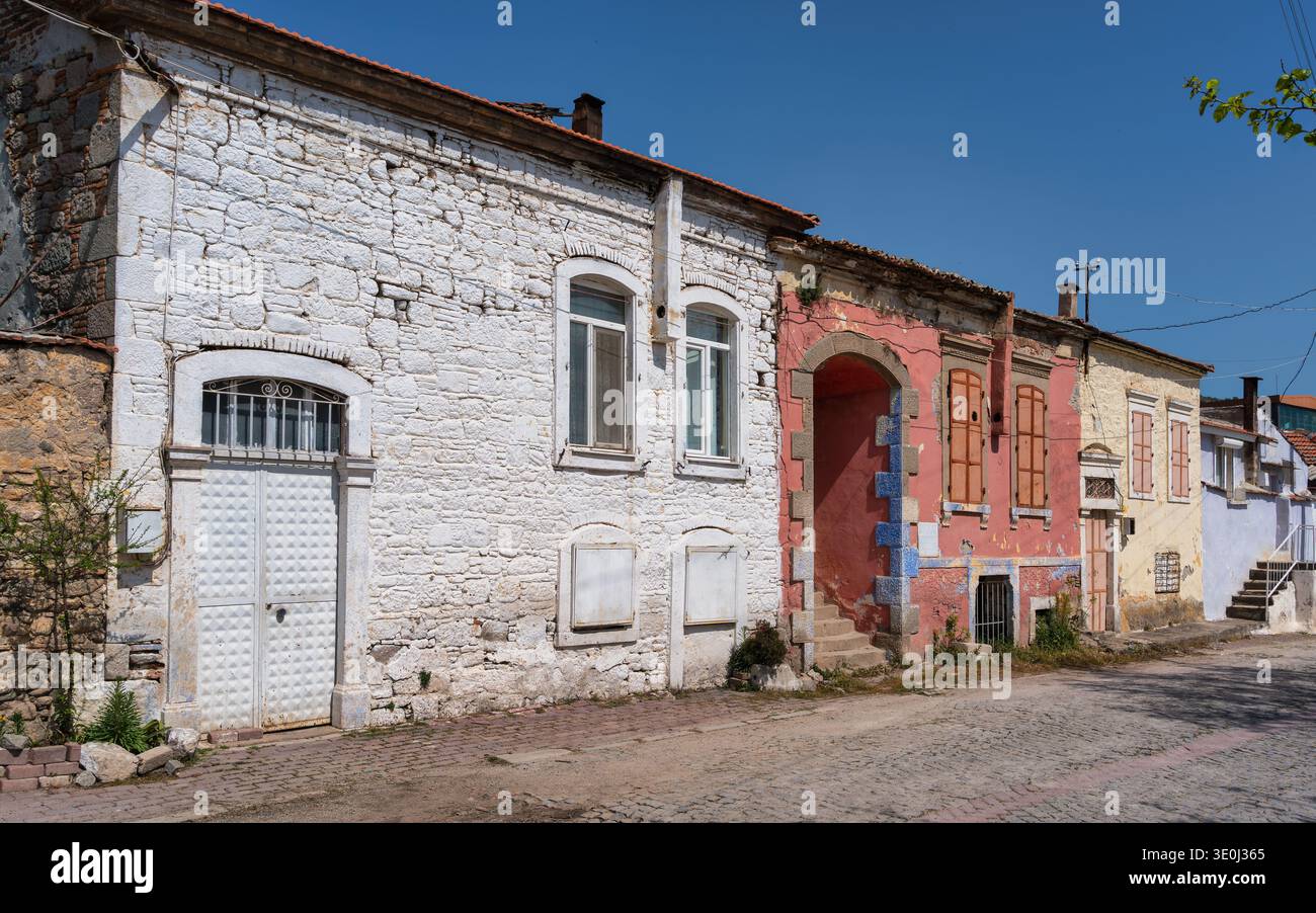 De vieilles maisons bordent une rue pavée dans un village. Certaines maisons ont des murs colorés, et beaucoup montrent des signes d'âge. Le soleil brille brillamment au-dessus, soulignant les structures simples. Banque D'Images