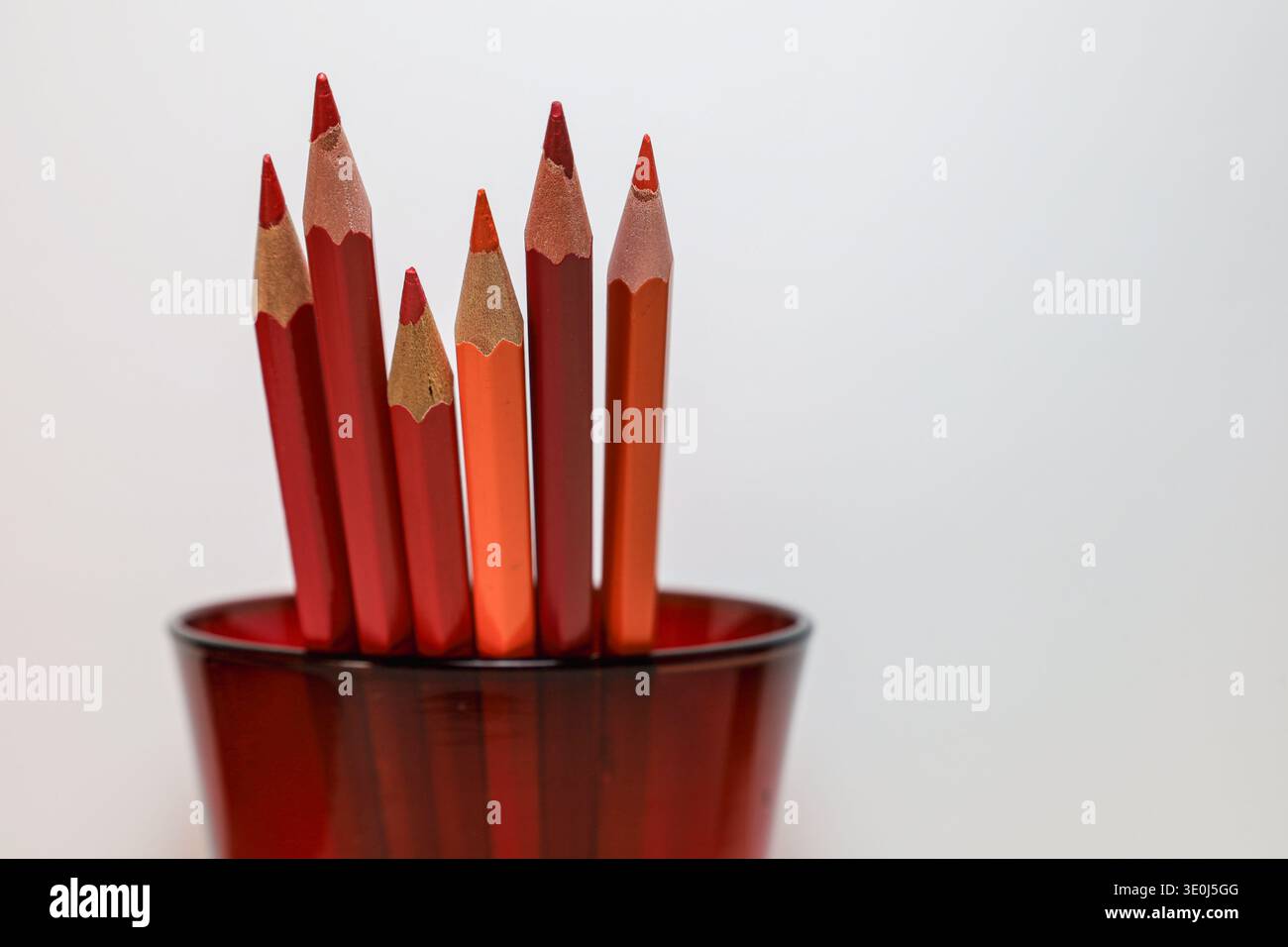 Ensemble de crayons de couleur rouge et orange disposés dans un support en verre translucide avec espace de copie propre, idéal pour l'éducation, la créativité et les concepts artistiques. Banque D'Images