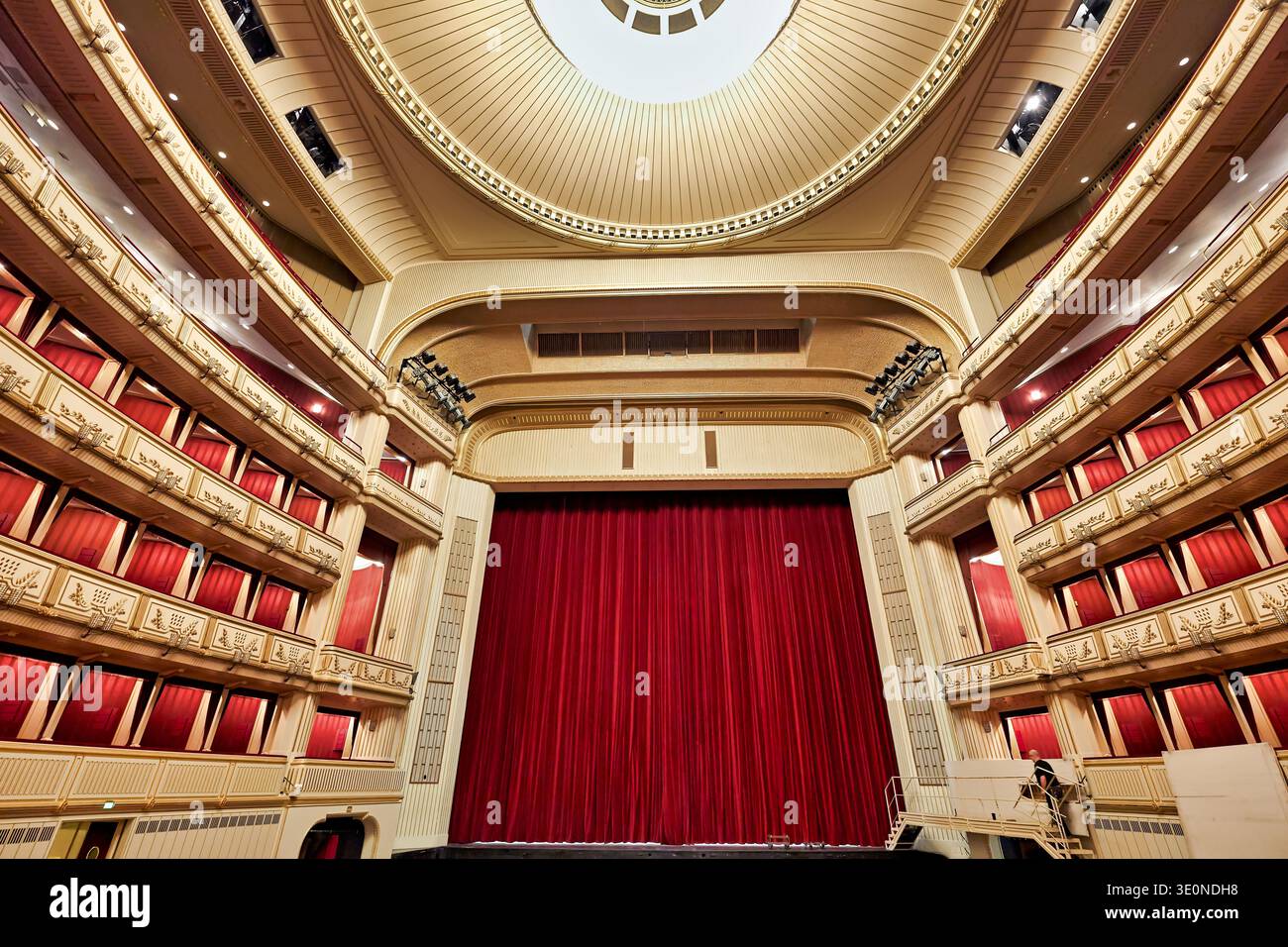 Une main de scène marche près du rideau rouge de l'Opéra national de Vienne. Le lieu est prêt pour le prochain spectacle avec sièges et balcons. Banque D'Images